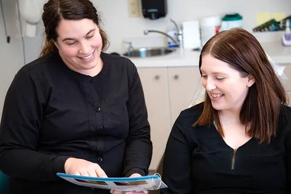 Two dental staff members in black scrubs smiling while reviewing a patient informational pamphlet together