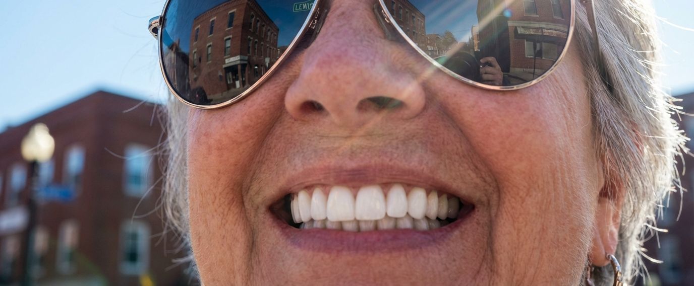 senior woman wearing sunglasses, smiling with bright white dentures